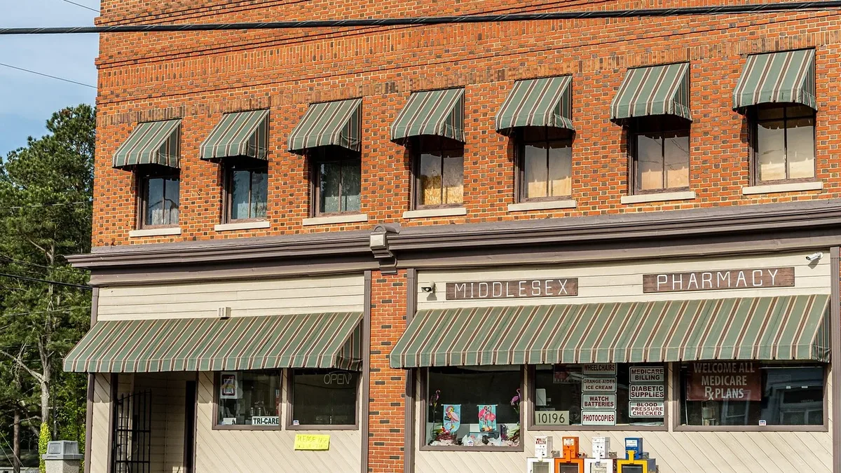 A two-story brick building with a pharmacy on the ground floor, featuring a sign that reads "MIDDLESEX PHARMACY" and a row of windows with green awnings.