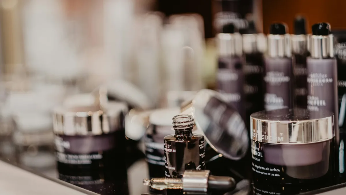 A collection of various bottles and jars of skincare products on a reflective surface, likely a counter or table.